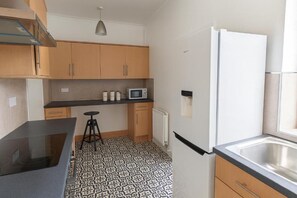 A compact kitchen with a microwave, a refrigerator, and a black countertop. - Coastal Haven - Steps From Beach (Whitehaven)