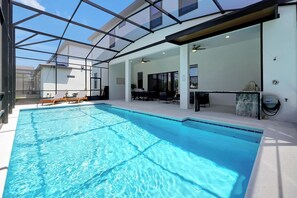 Ein Schwimmbecken mit Glaswänden, einem Deckenventilator und einer Sitzecke mit Tisch und Stühlen.