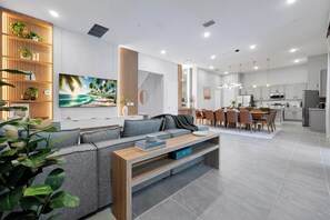 Ein modernes Wohnzimmer mit einer Couch, einem Couchtisch und einem Fernseher. Es gibt eine Küchenzeile mit einem Esstisch und Stühlen.