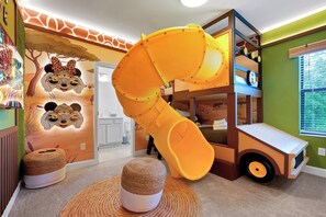 Ein Spielbereich für Kinder mit Rutsche, Stockbetten und einer Wand mit Giraffentier-Motiv.