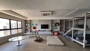 Un saló modern amb televisió, prestatges amb joguines, una zona de jocs i una finestra gran.