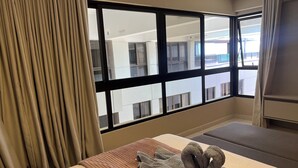 Habitació d'hotel amb una finestra gran, un llit, una taula de nit i vista de l'edifici exterior.