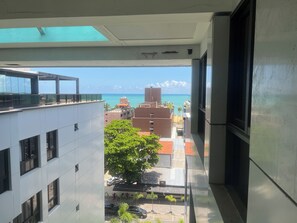 Blick vom Balkon auf eine Stadtlandschaft mit Gebäuden, einem Baum und wolkenlosem Himmel.