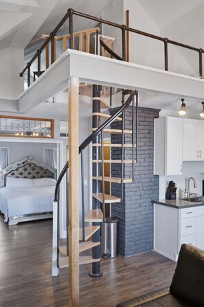 A modern loft-style bedroom with a large bed, a staircase, and a kitchen area. - Capitol Hill Retreat - Virtual Both units (Seattle)