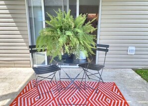 Eine Terrasse mit Tisch und Stühlen, einem Blumentopf und einem gemusterten Teppich.