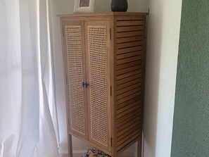 Ein Holzkabinent mit Lamellenüren, vor einer Wand mit einer grün gemusterten Oberfläche platziert.