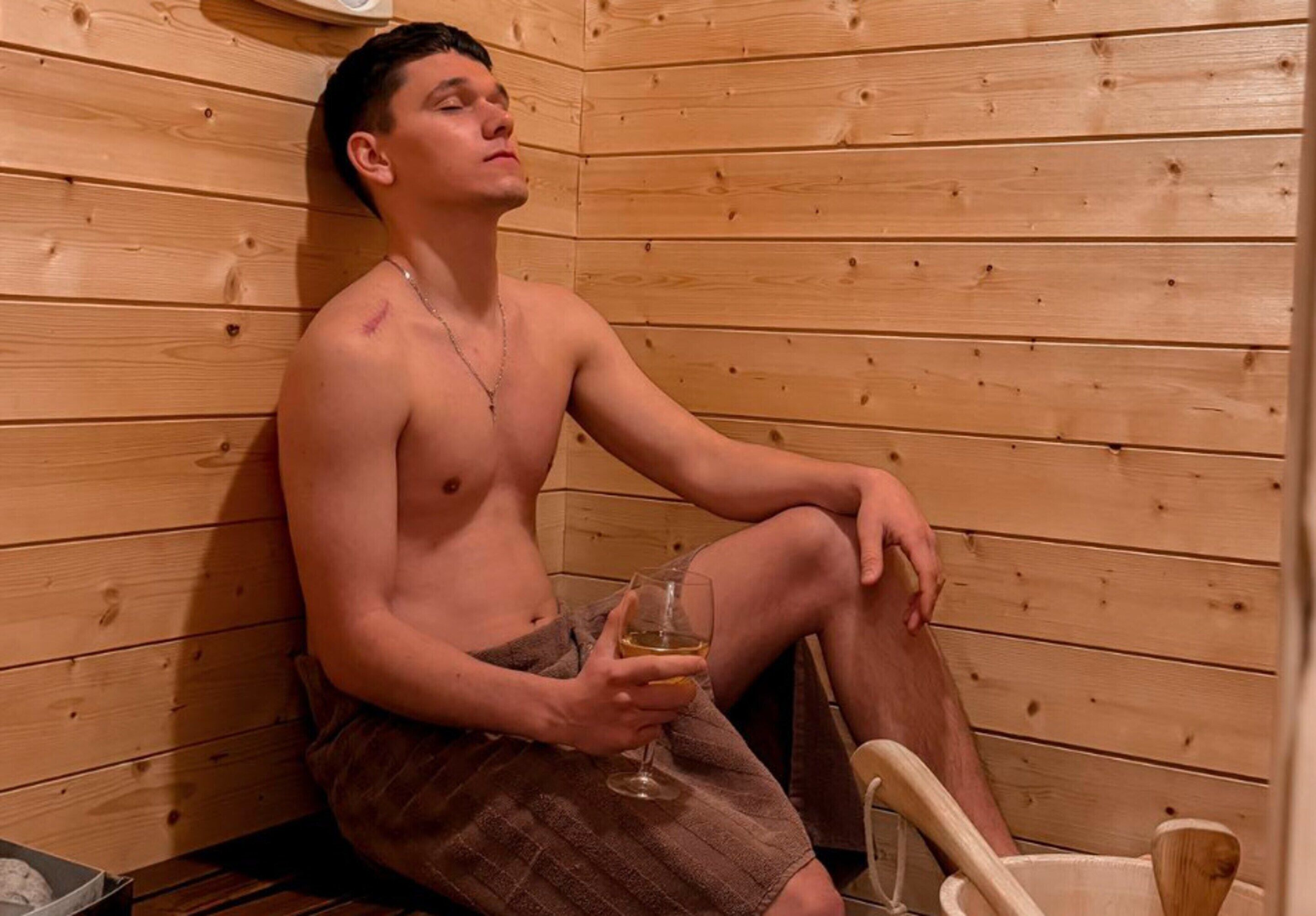 En person sitter i en bastu med träpanel och håller i ett glas.