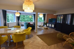 A modern living room with a dining area, large windows, and a television. - Comfortable Jacuzzi Apartment for 8 in Stezyca (gmina Stężyca)