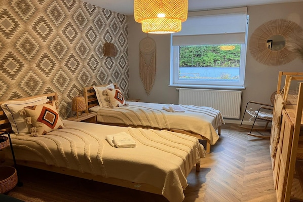 A room with two beds, a large window with a view of greenery, a hanging light fixture, and a wall with a geometric pattern. - Comfortable Jacuzzi Apartment for 8 in Stezyca (gmina Stężyca)