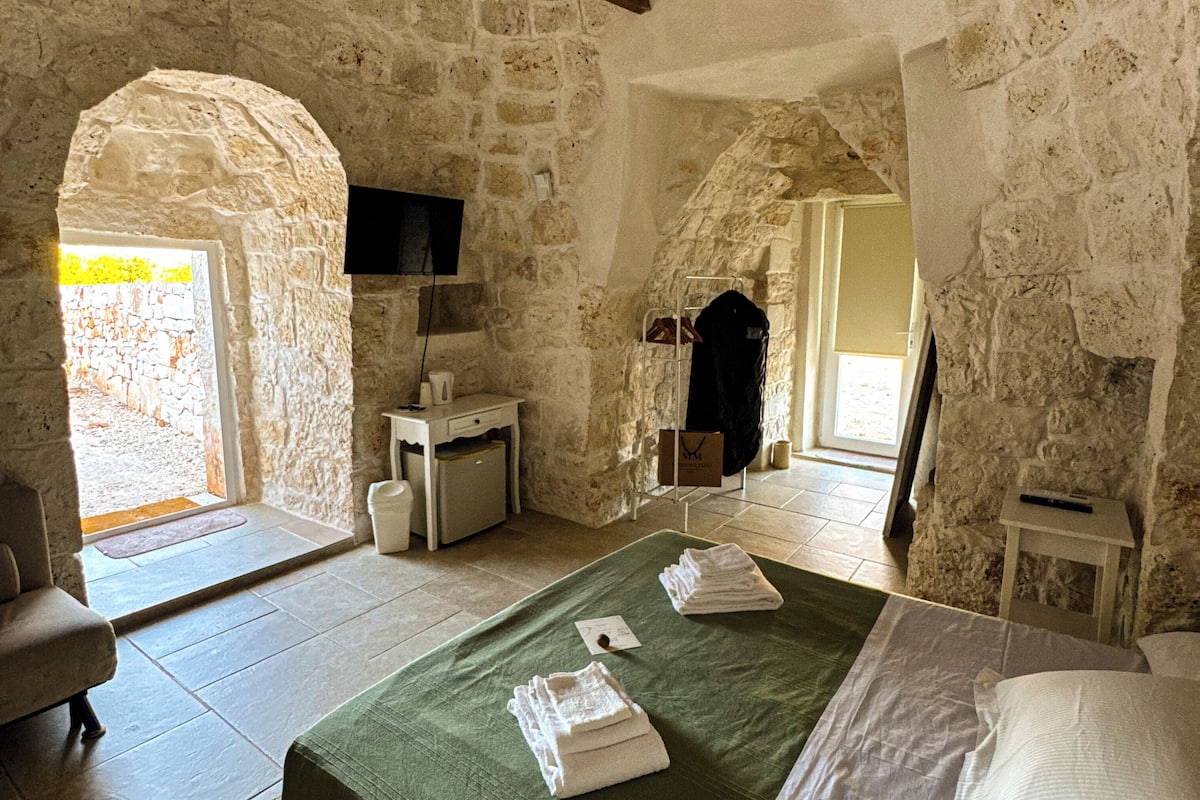 A stone-walled bedroom with a bed, a chair, a small table, and a television.