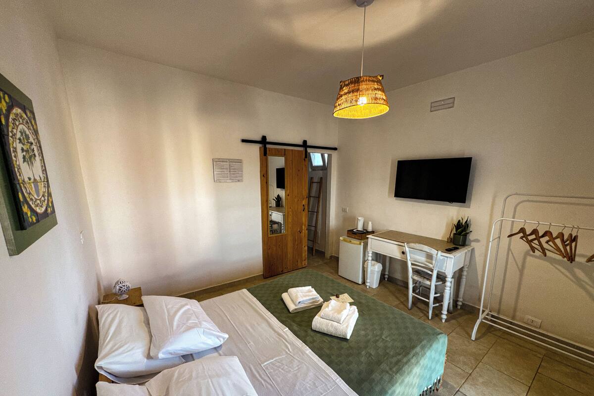 A hotel room with a bed, desk, chair, TV, and a hanging clothes rack.