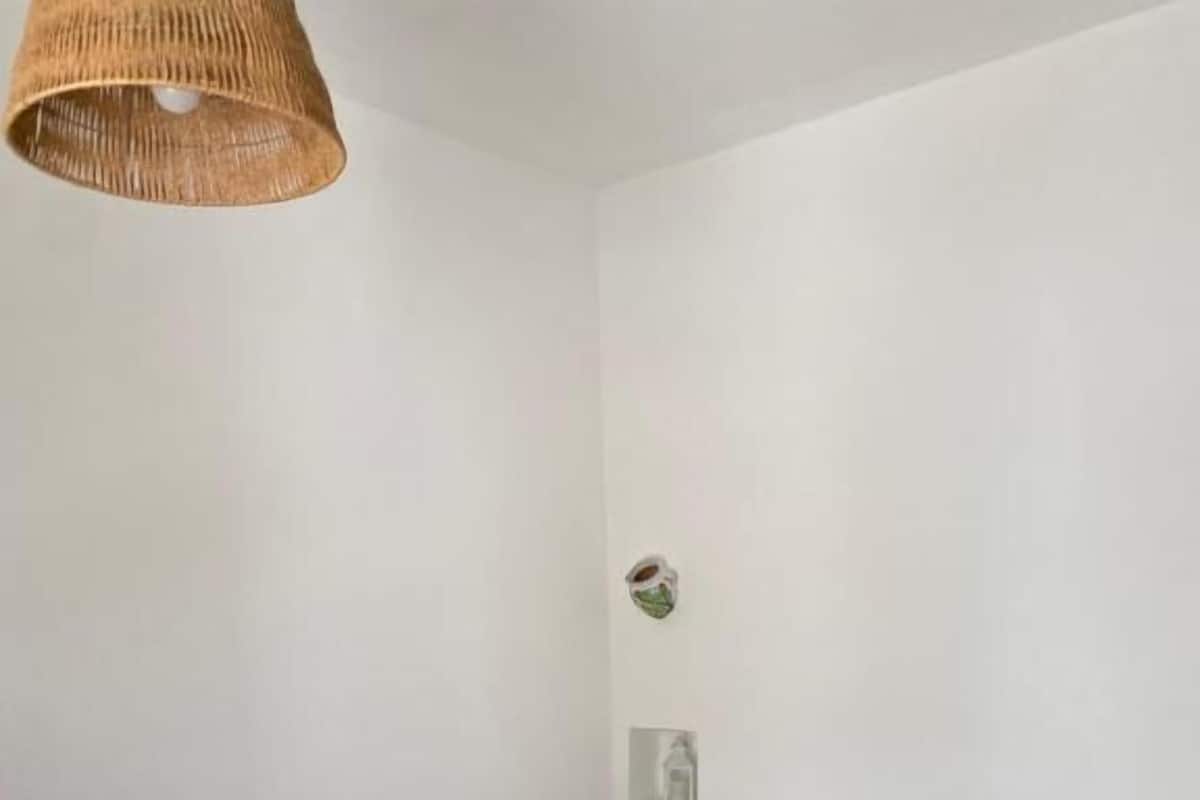 A single bed with a green bedspread and white pillows, a woven light fixture, and a small wall decoration.