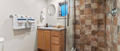 Un baño con cabina de ducha de vidrio, lavamanos con encimera de mármol, armarios de madera y dos toallas blancas con el logo 'AVANTSTAY'.