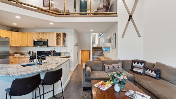 A modern kitchen with granite countertops, wooden cabinets, and stainless steel appliances. There is a dining area with a wooden table and chairs, and a living room with a sofa and a coffee table. - Telluride Lodge 518 by Avantstay Communal Hot Tub + Sauna + Mountain Views Steps to Gondola (Telluride)