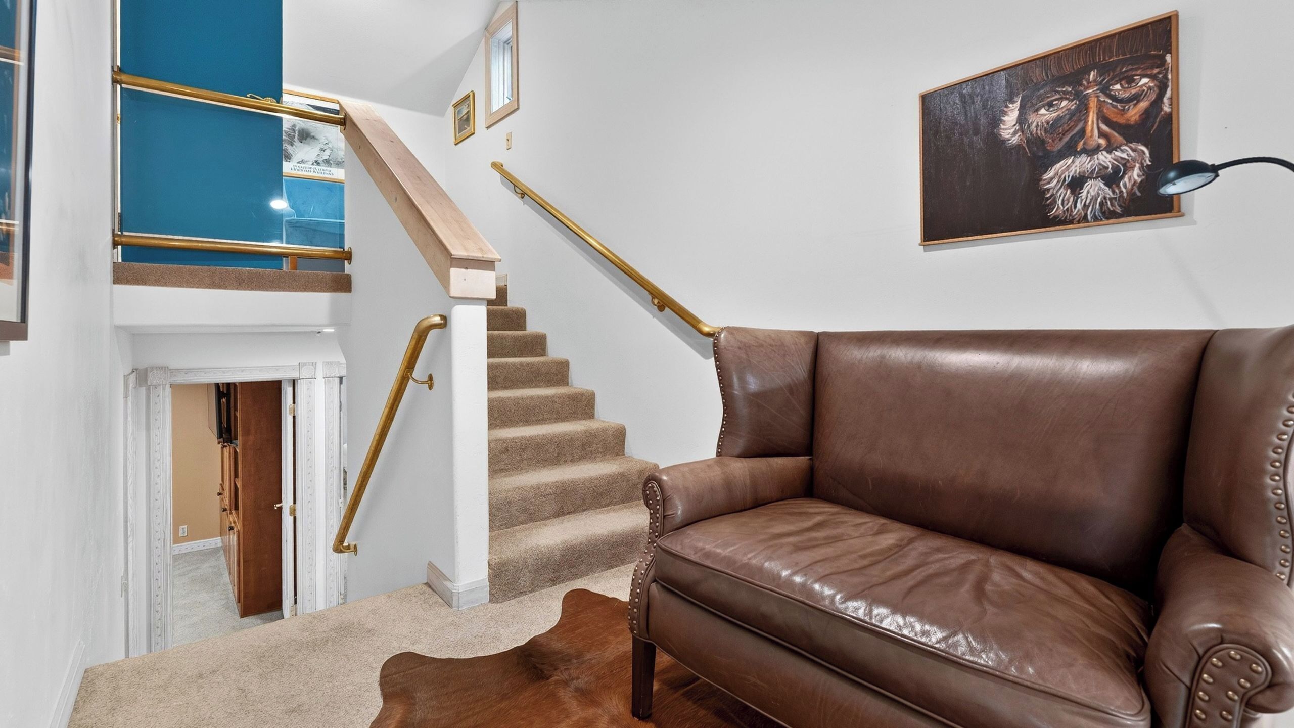 A staircase with a golden handrail, a brown leather sofa, a framed artwork, and a cowhide rug.