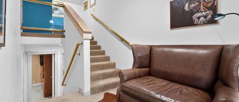 A staircase with a golden handrail, a brown leather sofa, a framed artwork, and a cowhide rug.