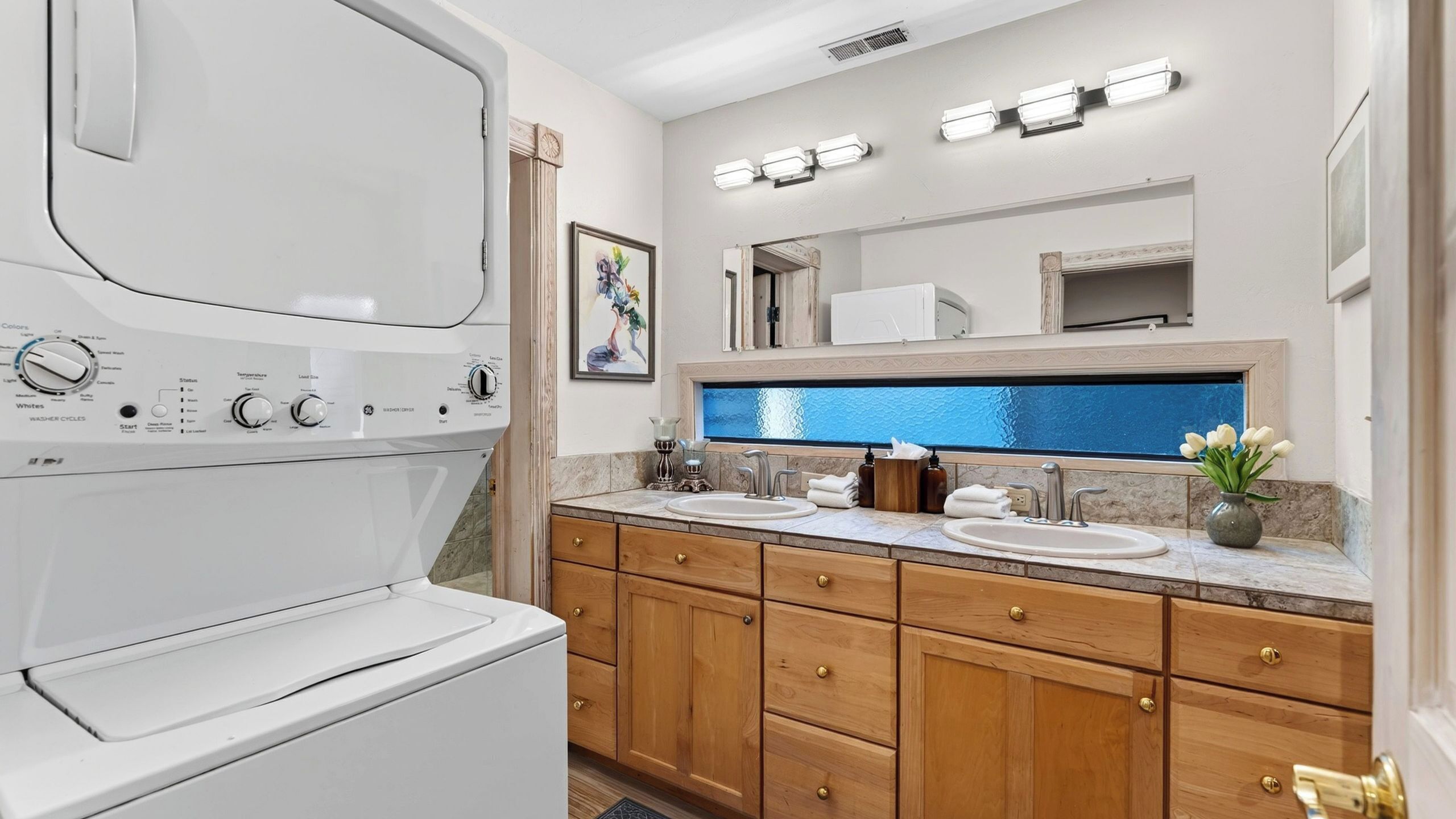A modern bathroom with a built-in washer and dryer, dual sinks, wooden cabinets, and a large mirror.