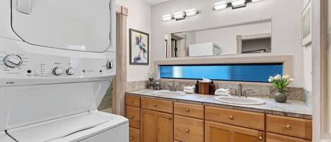 A modern bathroom with a built-in washer and dryer, dual sinks, wooden cabinets, and a large mirror.