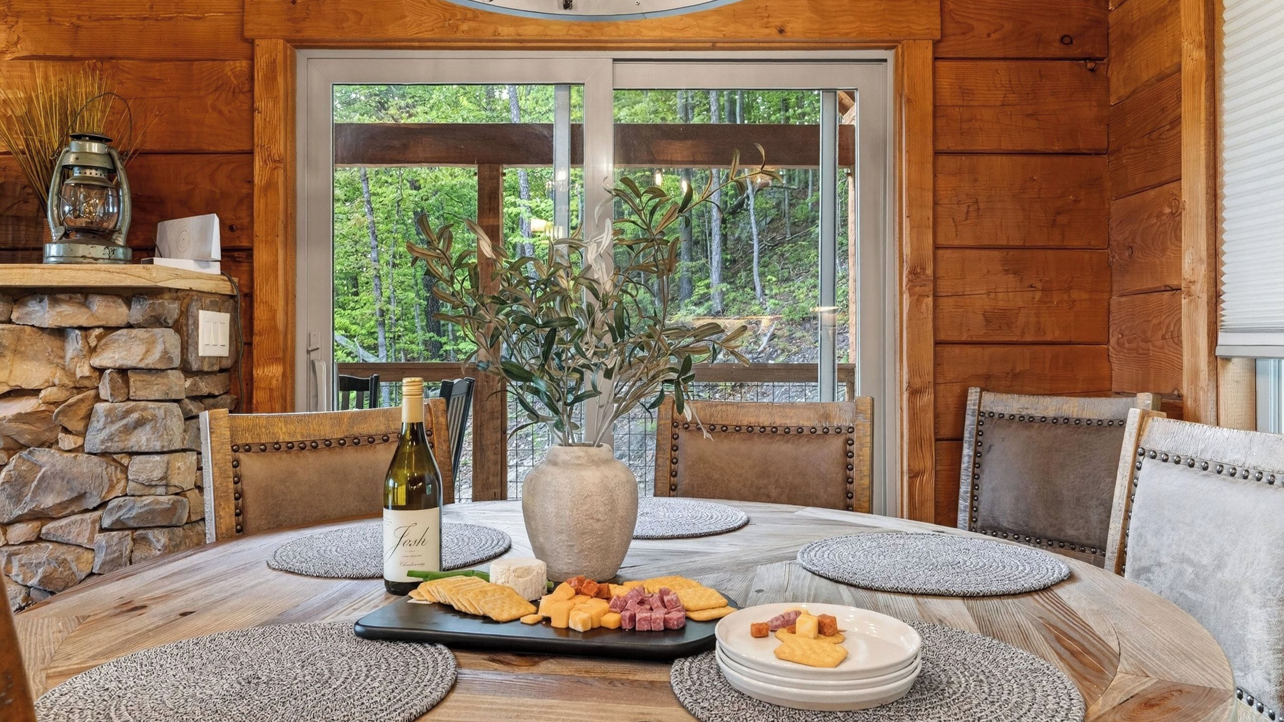 A wooden interior with a stone wall, a table set with food, and a view of greenery outside.