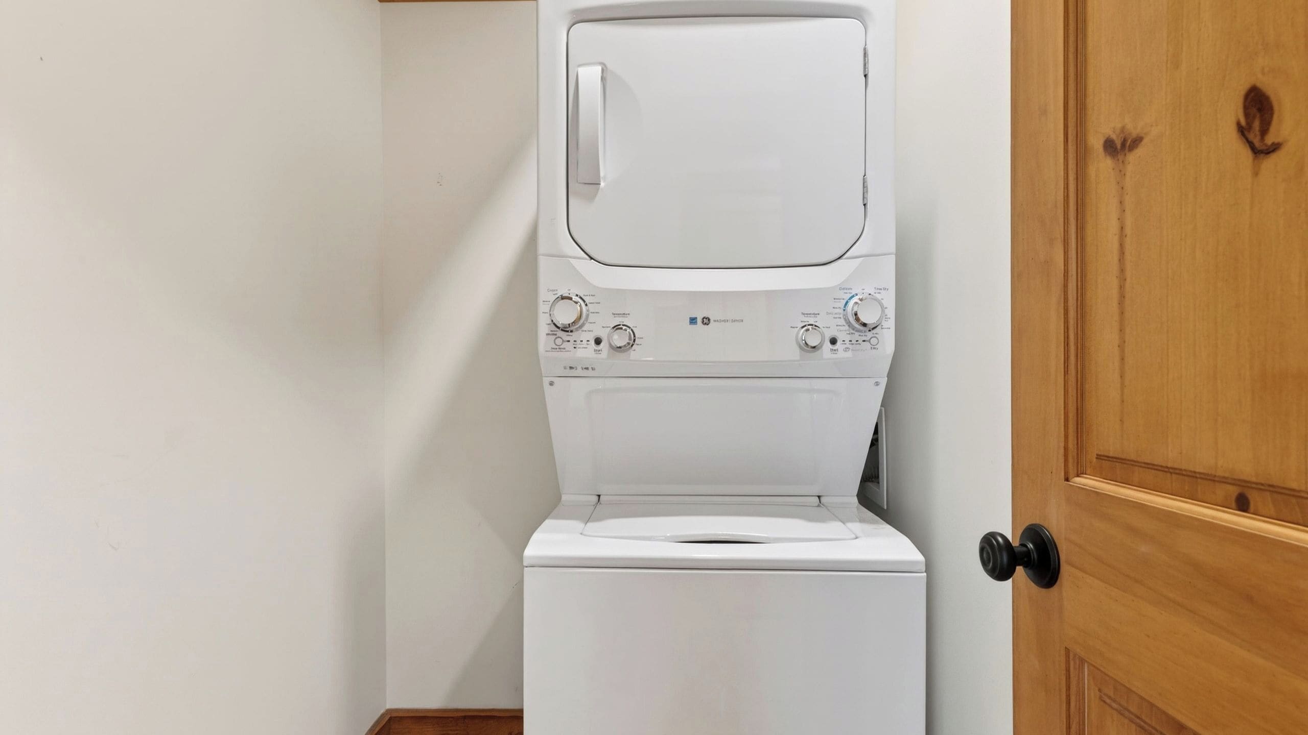 Un appareil combiné lave-linge et sèche-linge blanc, doté de boutons de commande et d’une porte en bois.