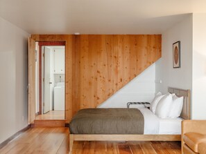 A bedroom with a wooden sloped ceiling, a bed with white bedding, and a wooden floor. - Blue Whale Cove | Cliffside Ocean Views (Whitethorn)