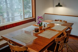 A dining table with four chairs, a vase with flowers, salt and pepper shakers, and a hanging light fixture. - Blue whale cove | Cliffside Ocean Views | Hot tub (Whitethorn)