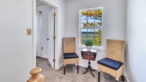 Habitación de esquina con ventana, puerta y dos sillones de mimbre con cojines oscuros.