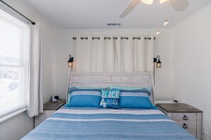 Ein Schlafzimmer mit einem Bett, Nachttischen, einem Deckenventilator und einem Fenster mit Jalousien.