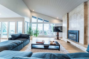 Una sala de estar moderna con sofá, mesa de centro, televisor, chimenea y ventanas amplias.