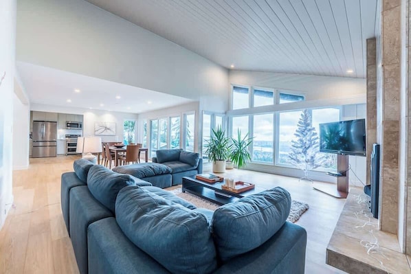 Una sala de estar moderna con un sofá seccional, un comedor, una cocina y un ventanal con vistas.