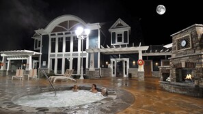 A building with a large outdoor hot tub area, a stone fireplace, and a moon in the sky.