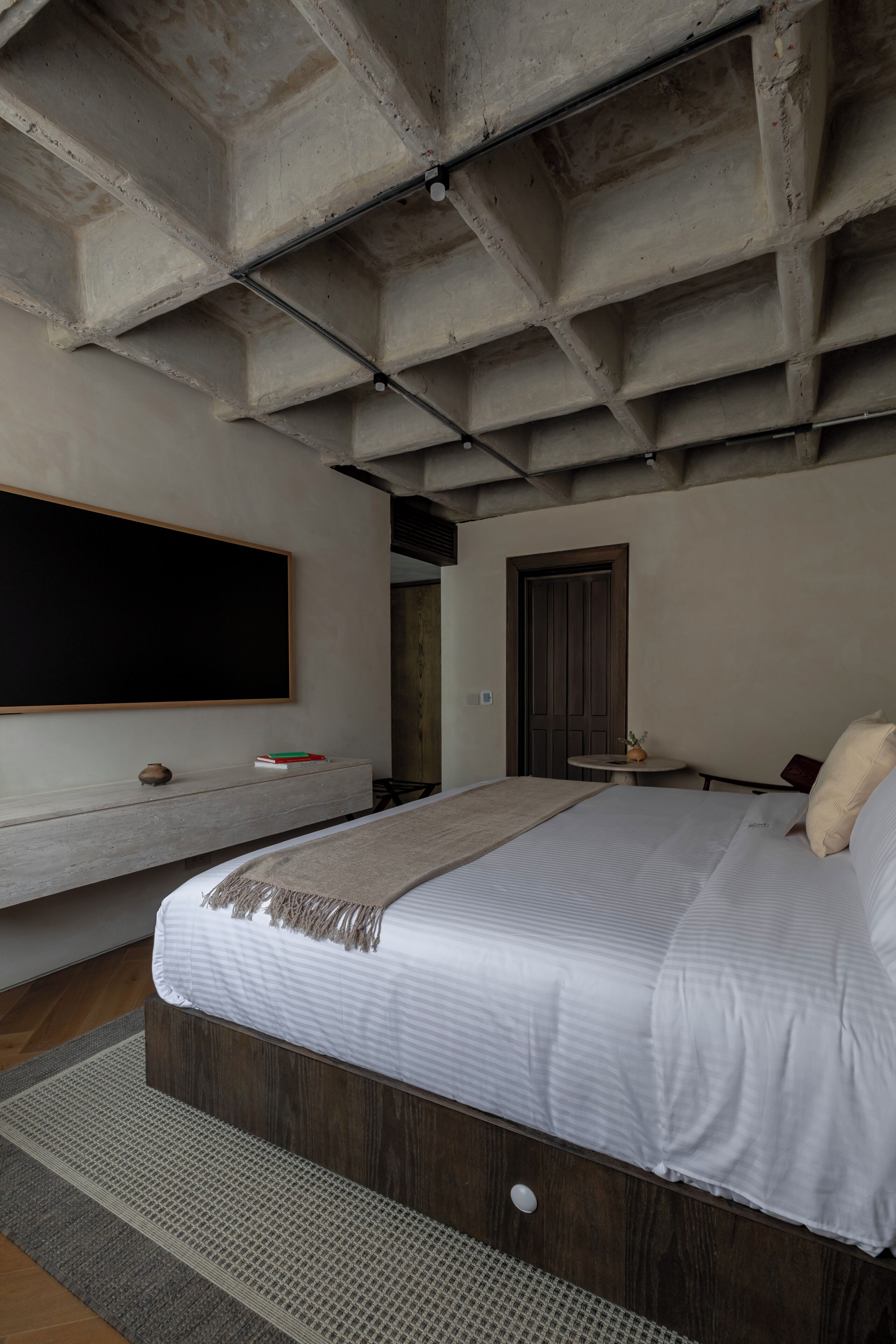 Una camera da letto moderna con un letto grande, una TV a muro, una porta in legno e un tavolino con un vaso.