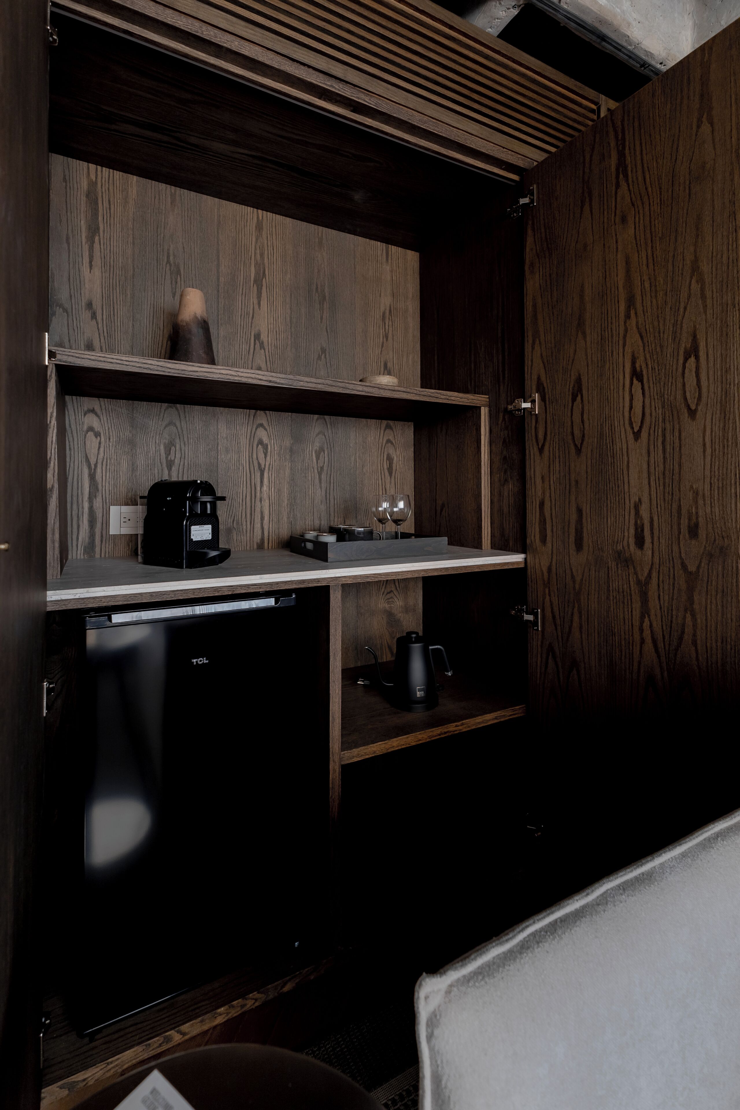Une cuisine compacte équipée d’une machine à café, de verres à vin et d’une bouilloire, le tout posé sur un plan de travail en bois.