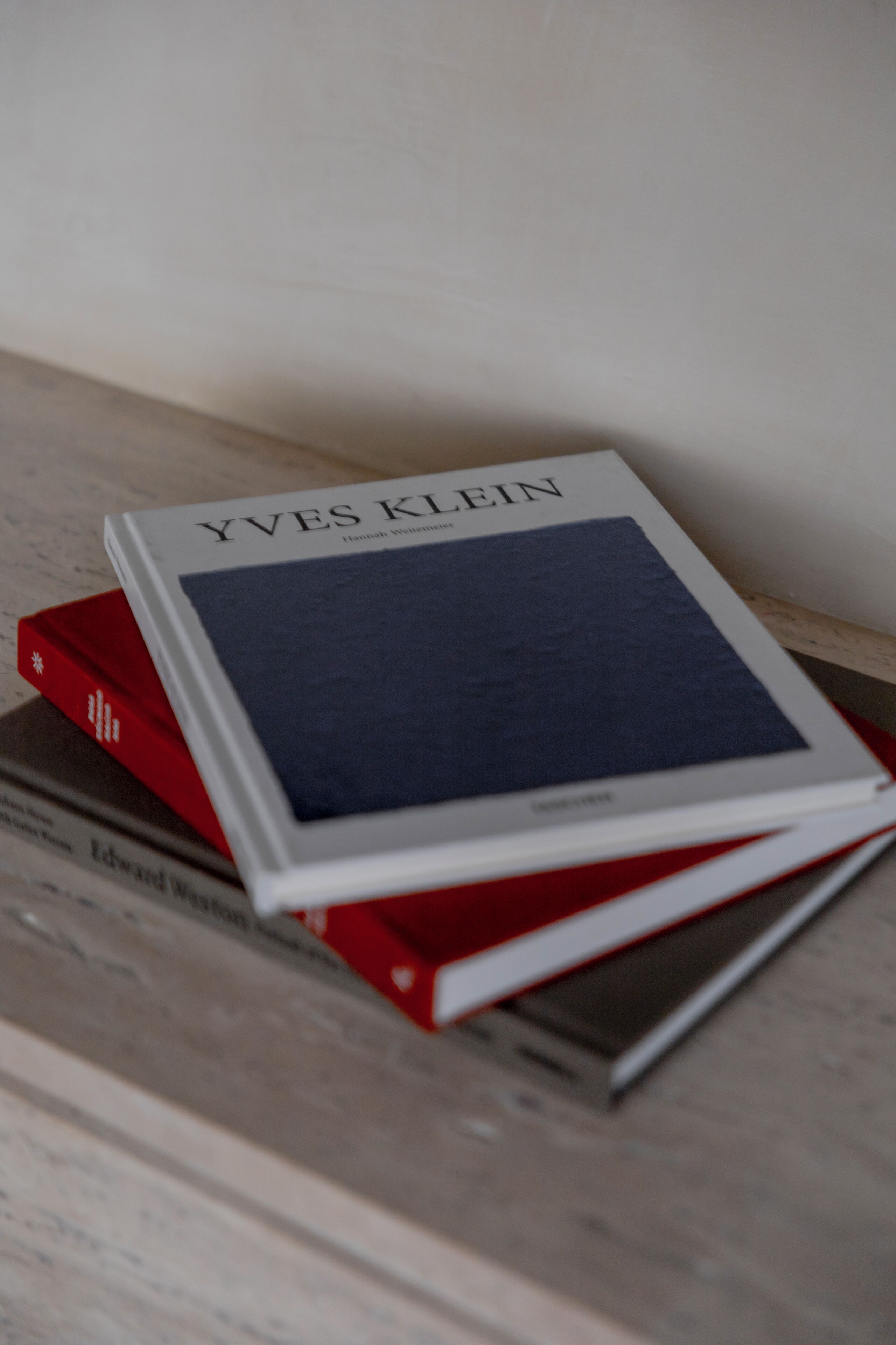 A stack of books with one titled 'Yves Klein' on a shelf.