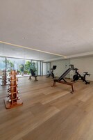 A spacious gym with wooden flooring, exercise equipment, and large windows offering views of the city.