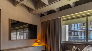 Un salon moderne comprenant un canapé, une table d’appoint, une lampe, une grande fenêtre avec des rideaux et un miroir fixé au mur.