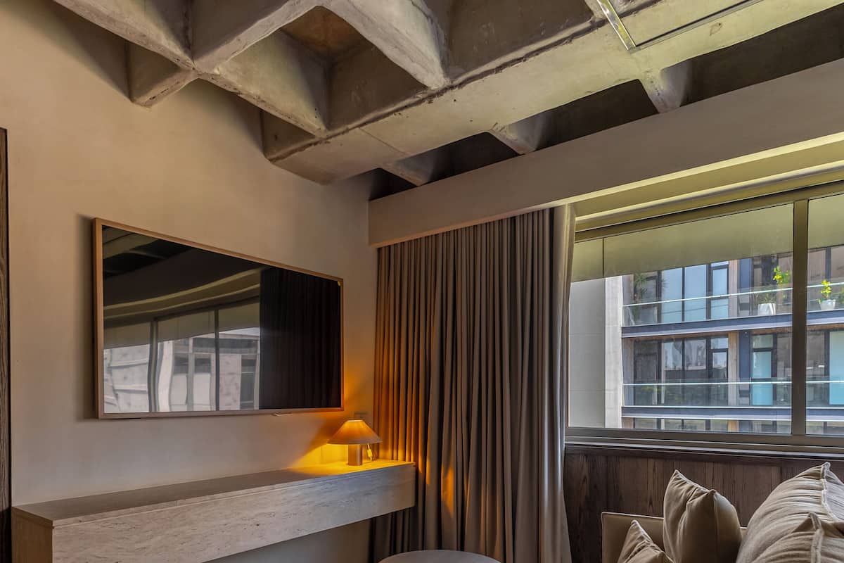 Un salon moderne comprenant un canapé, une table d’appoint, une lampe, une grande fenêtre avec des rideaux et un miroir fixé au mur.