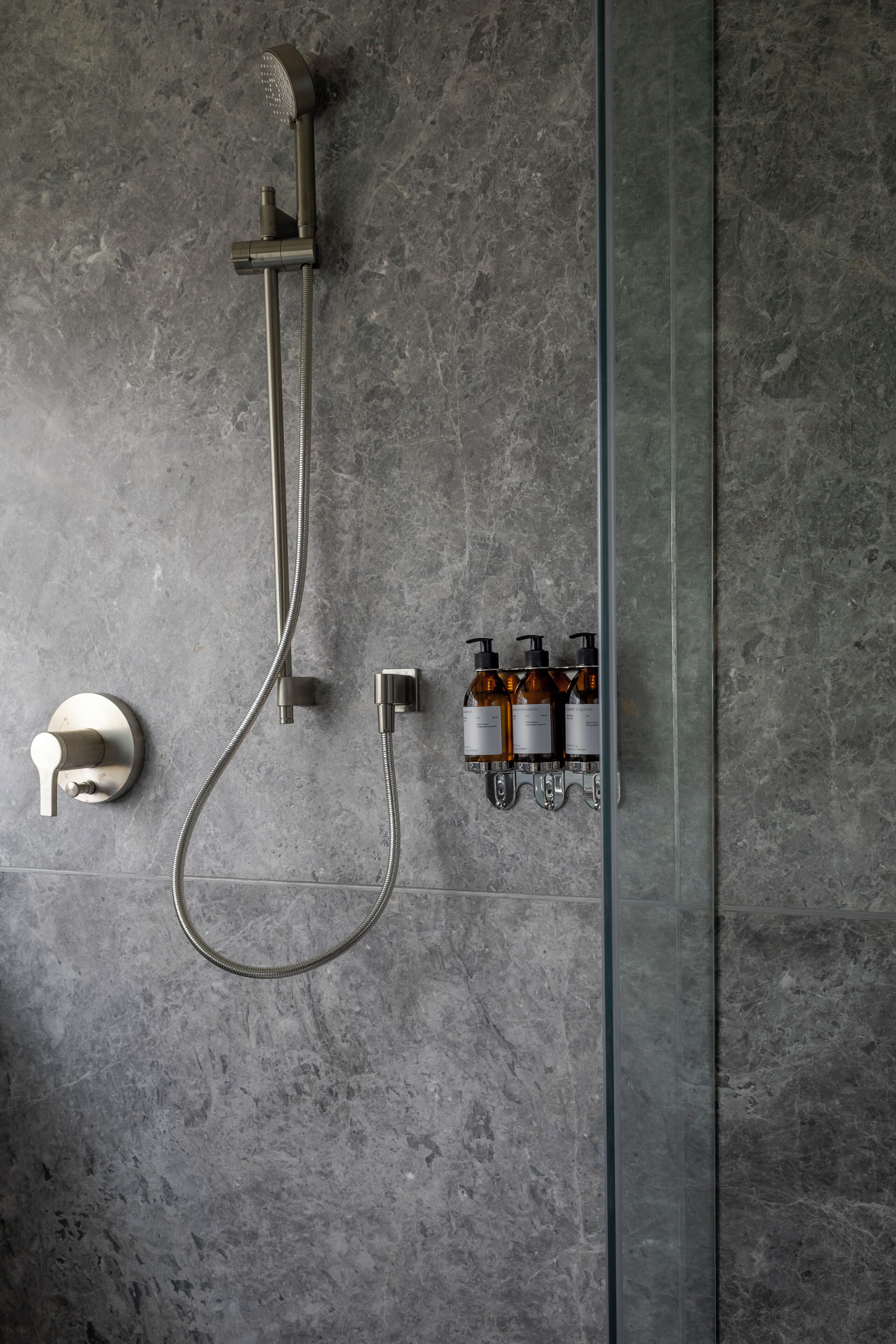A shower with a handheld showerhead, a wall-mounted faucet, and a soap dispenser mounted on the wall.