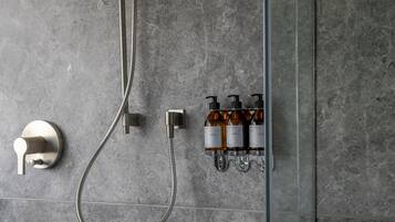 A shower with a handheld showerhead, a wall-mounted faucet, and a soap dispenser mounted on the wall.