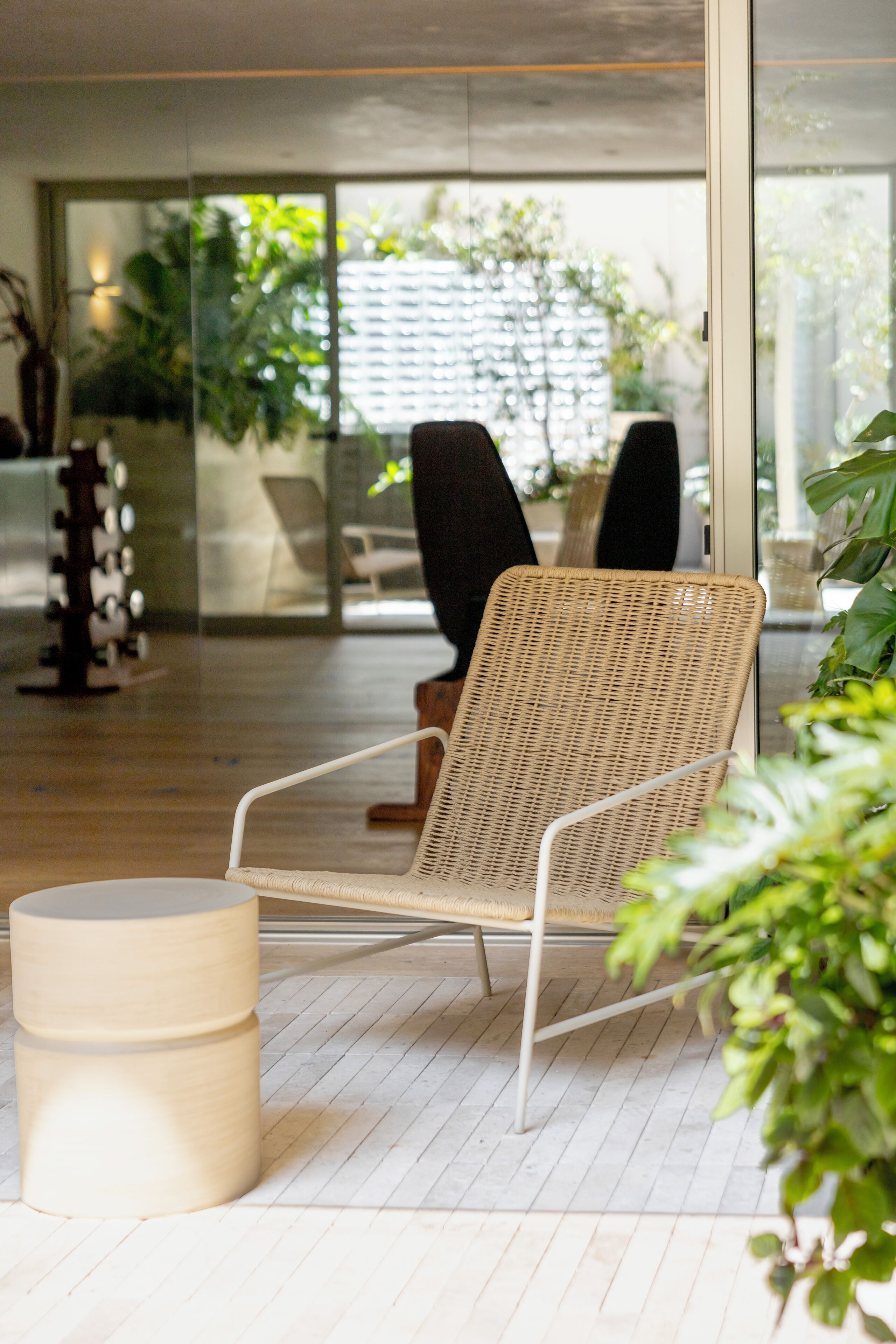 A modern lounge area with a wicker chair, a small round table, and a glass partition.