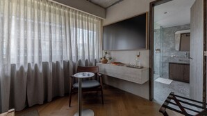 Une chambre moderne avec un plancher en bois, une table ronde avec une chaise, un grand miroir et une vue sur une salle de bain par une porte ouverte.