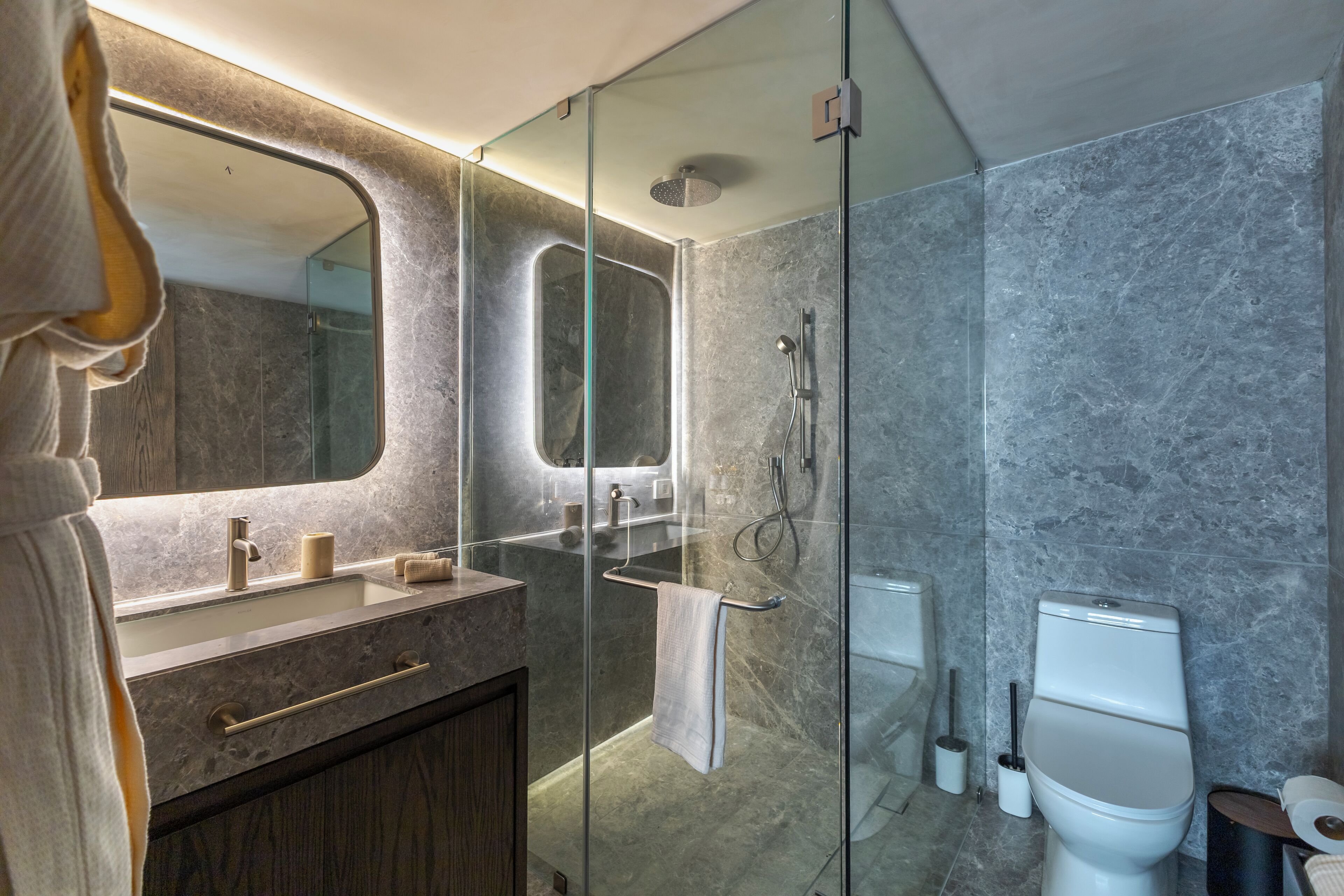 Un baño moderno con ducha de vidrio, lavamanos de mármol y retrete.