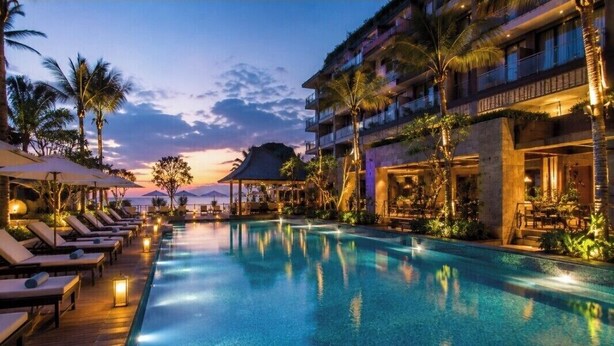 A poolside area with lounge chairs, a pool, and a building with balconies.