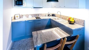 A modern kitchen with blue cabinets, a microwave, a sink, a black pendant light, and a fruit bowl on the counter. - Premium Dziwnow Coastal Apartment for 3 (Dziwnów)