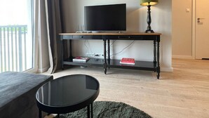 A room with a television on a wooden console table, a lamp, a small round table, and a sofa. - Premium Dziwnow Coastal Apartment for 3 (Dziwnów)