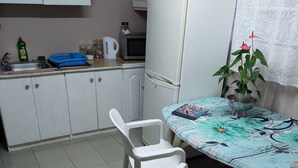 A small kitchen with white cabinets, a microwave, and a sink. There is a table with chairs and a potted plant.
