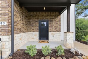 A brick building with a black door, a stone base, and a doormat with the word 'howdy'. - Gathering Home - Sleeps 10 - 4 King Beds 4.5 Baths (College Station)