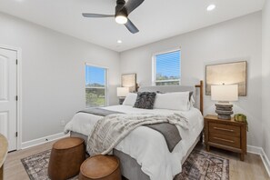 A bedroom with a bed, two bedside tables, a ceiling fan, and two windows with blinds. - Gathering Home - Sleeps 10 - 4 King Beds 4.5 Baths (College Station)