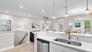 A modern kitchen with a dishwasher, stainless steel sink, pendant lights, and a dining area with a view. - Crystal Dream at 111 | Golf Cart & Bikes | Pool | Walk to Beach & Destin Commons (Destin)