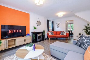 Een woonkamer met een flatscreen televisie, een bank, een salontafel en een open haard.